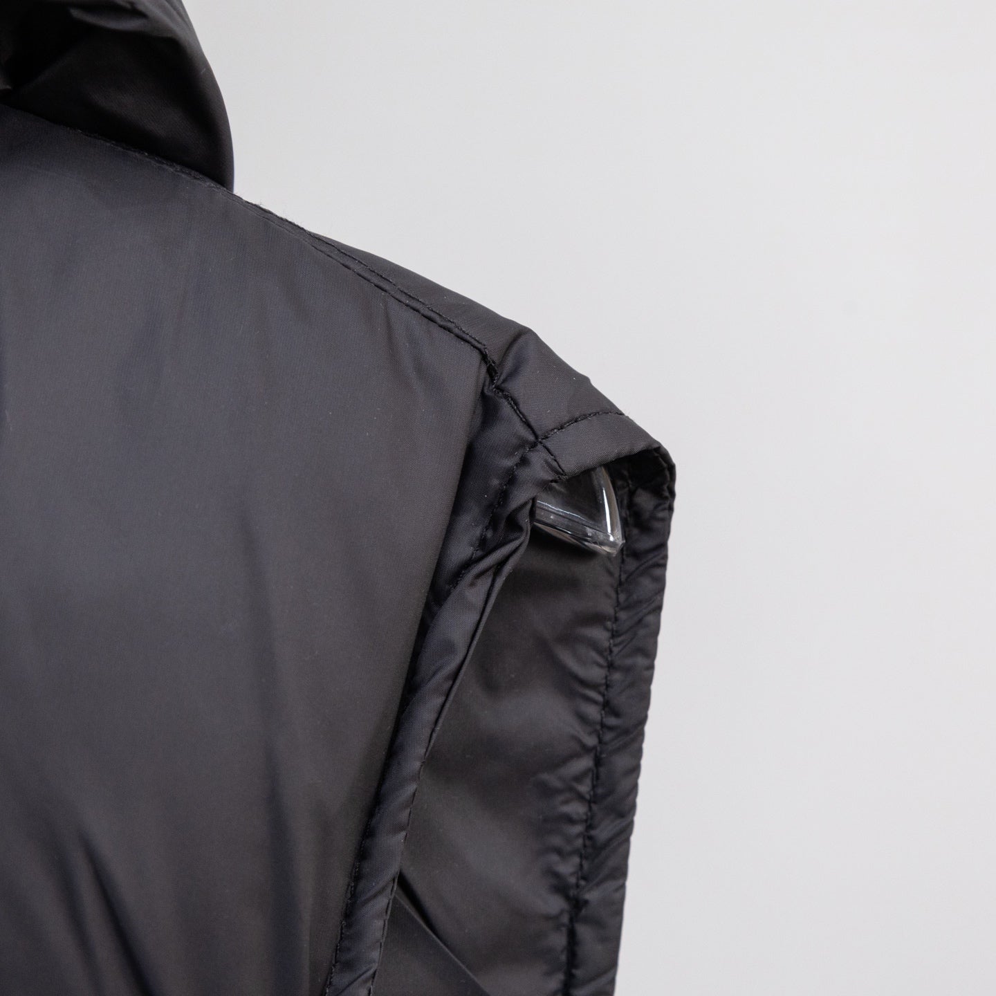 Black quilted puffer vest with hood, stitched shoulder panel, and visible cuff seam