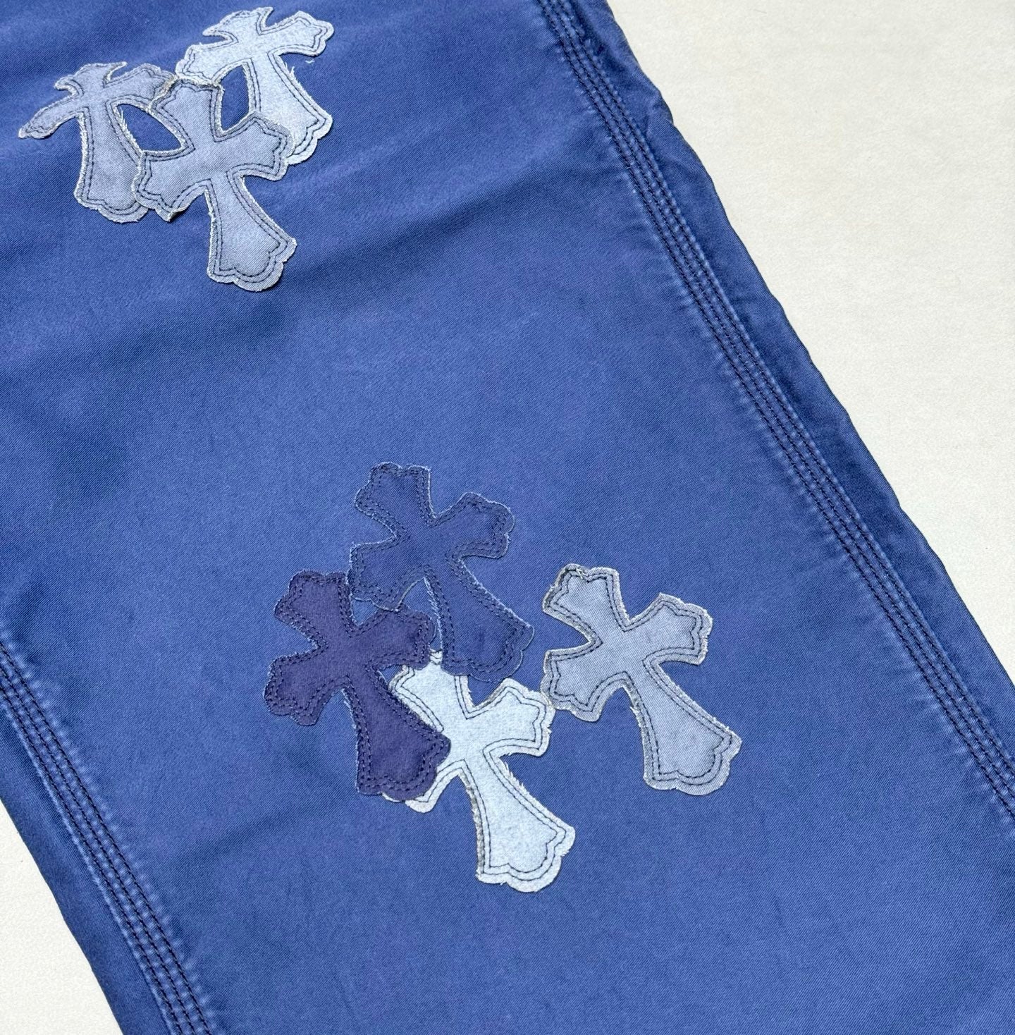 Blue pants leg with embroidered cross appliques in gray thread