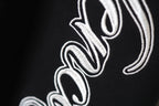 Black fabric with close-up white embroidered script logo on leg