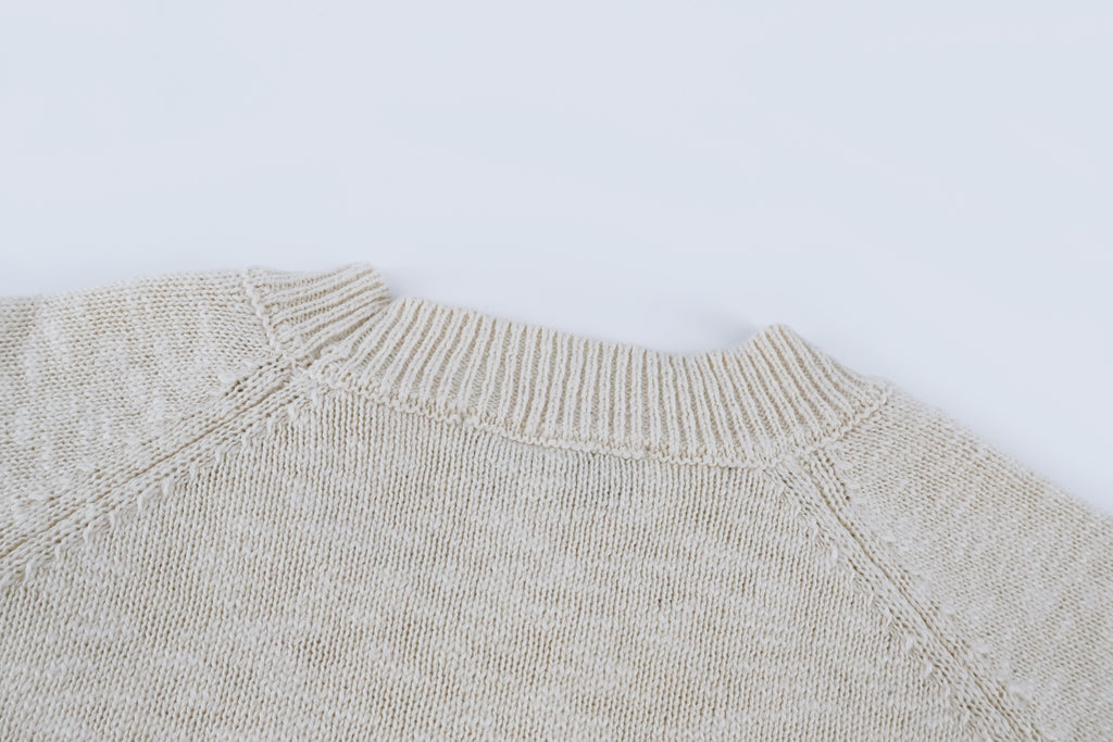 Light beige knit sweater shoulder and neckline close-up, ribbed collar