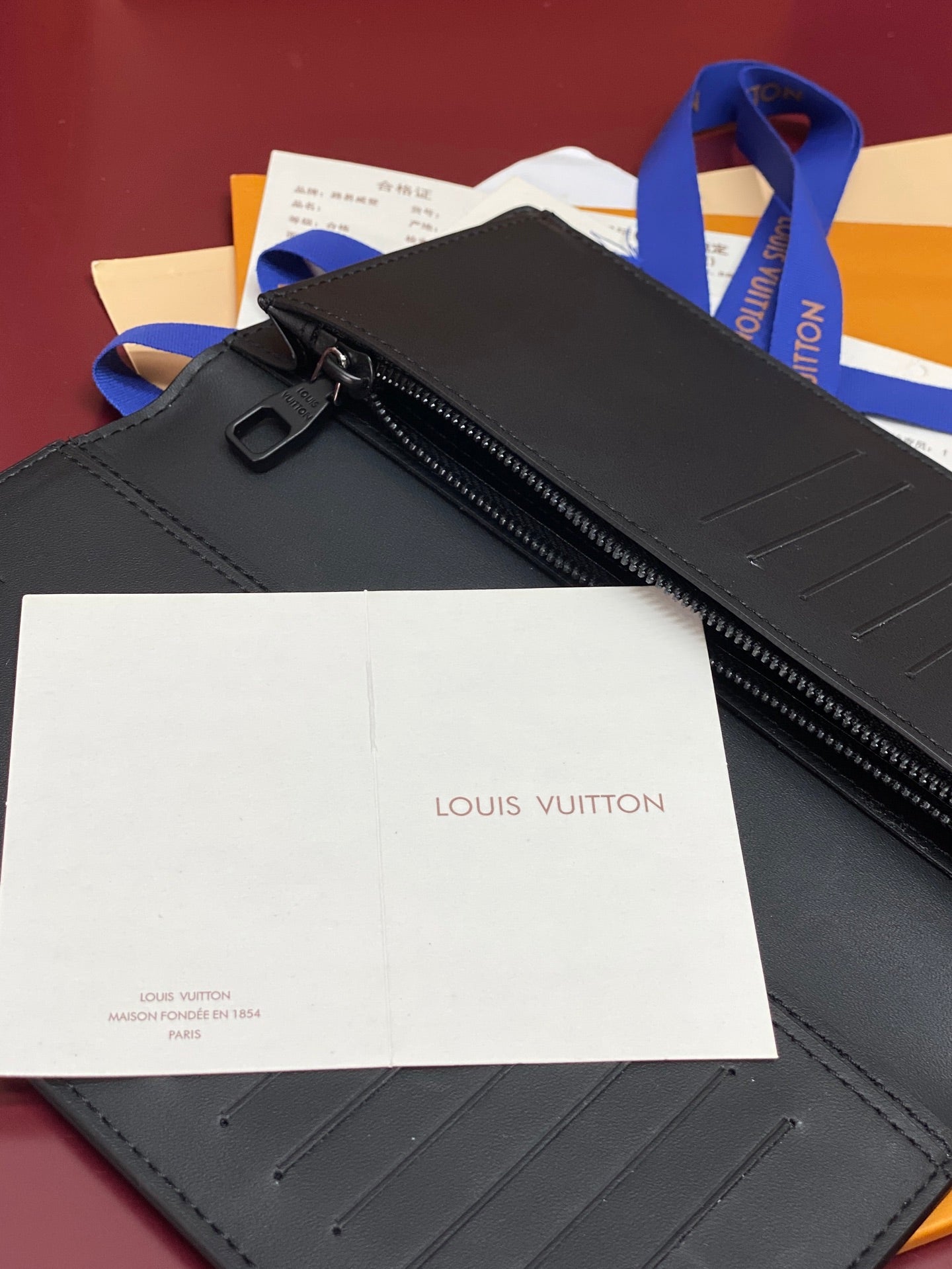 Small wallet bag with zip top and blue strap, shown with dust bag and label