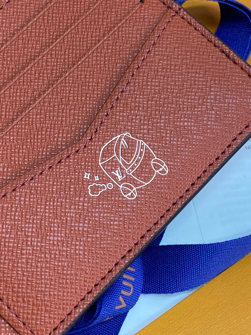 Small bi-fold card wallet close-up of embossed emblem on tan leather