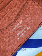Small bi-fold card wallet close-up of printed Louis Vuitton Paris text on tan leather