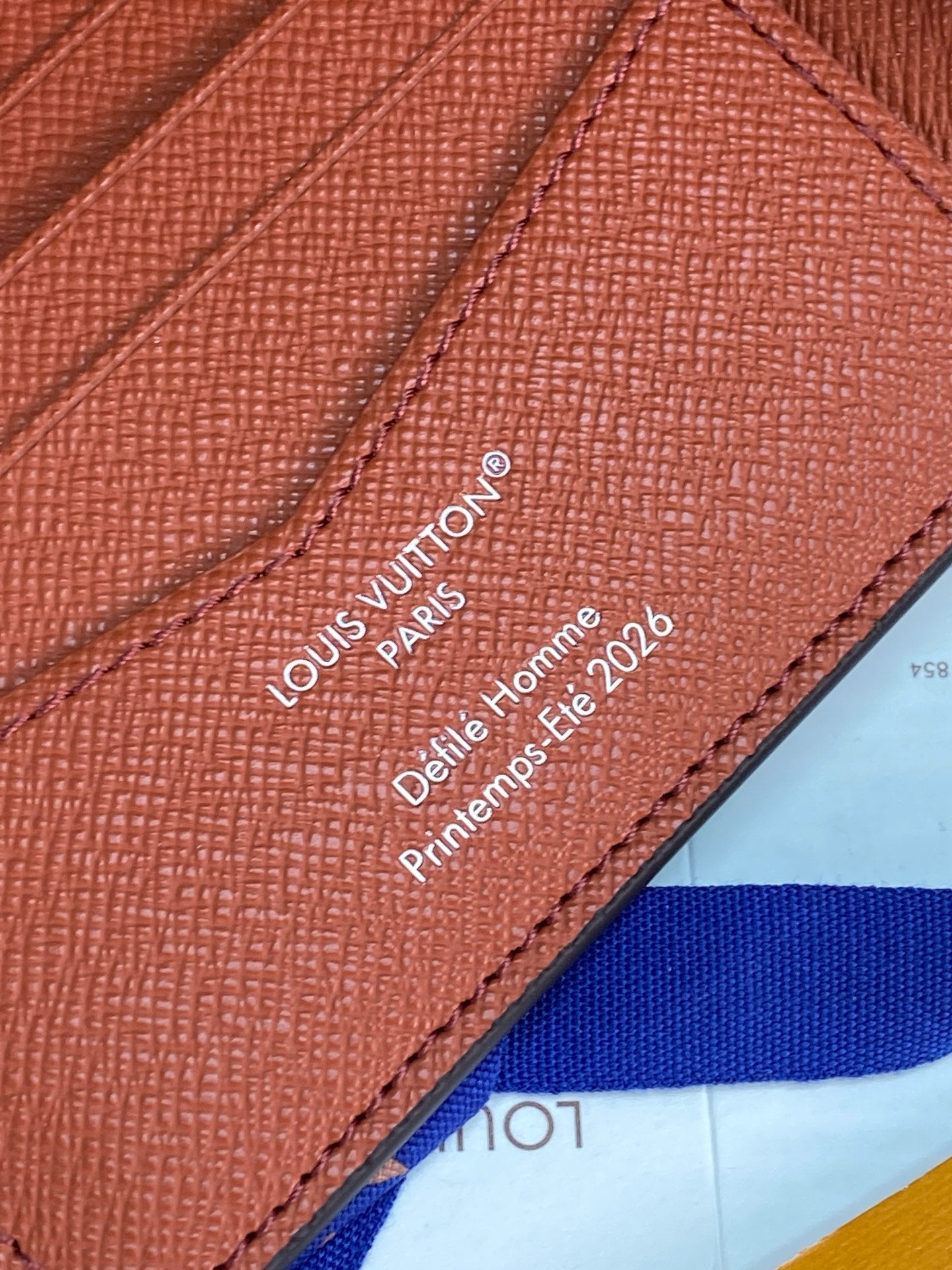 Small bi-fold card wallet close-up of printed Louis Vuitton Paris text on tan leather