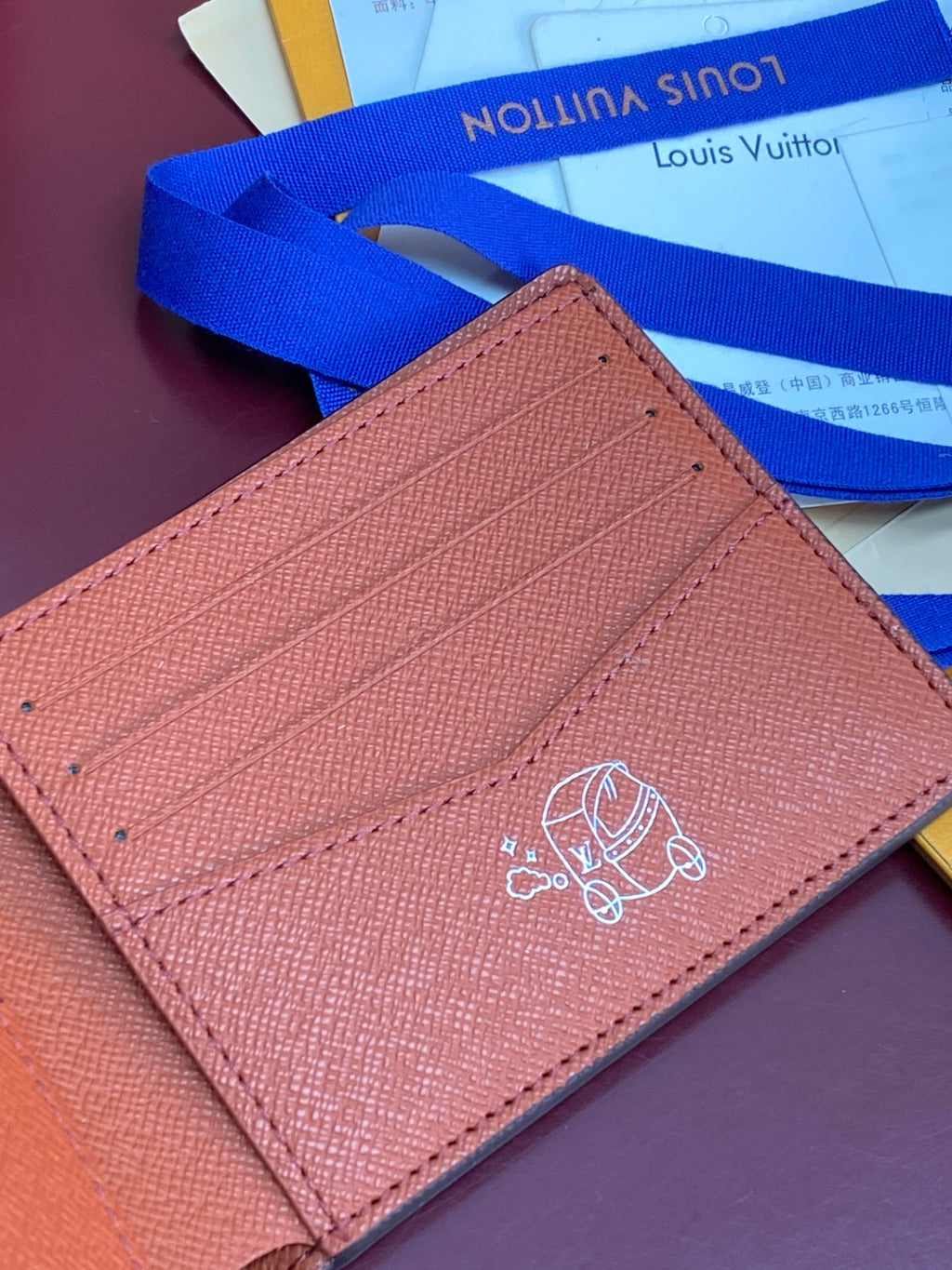 Small bi-fold card wallet close-up, tan leather with embossed crest