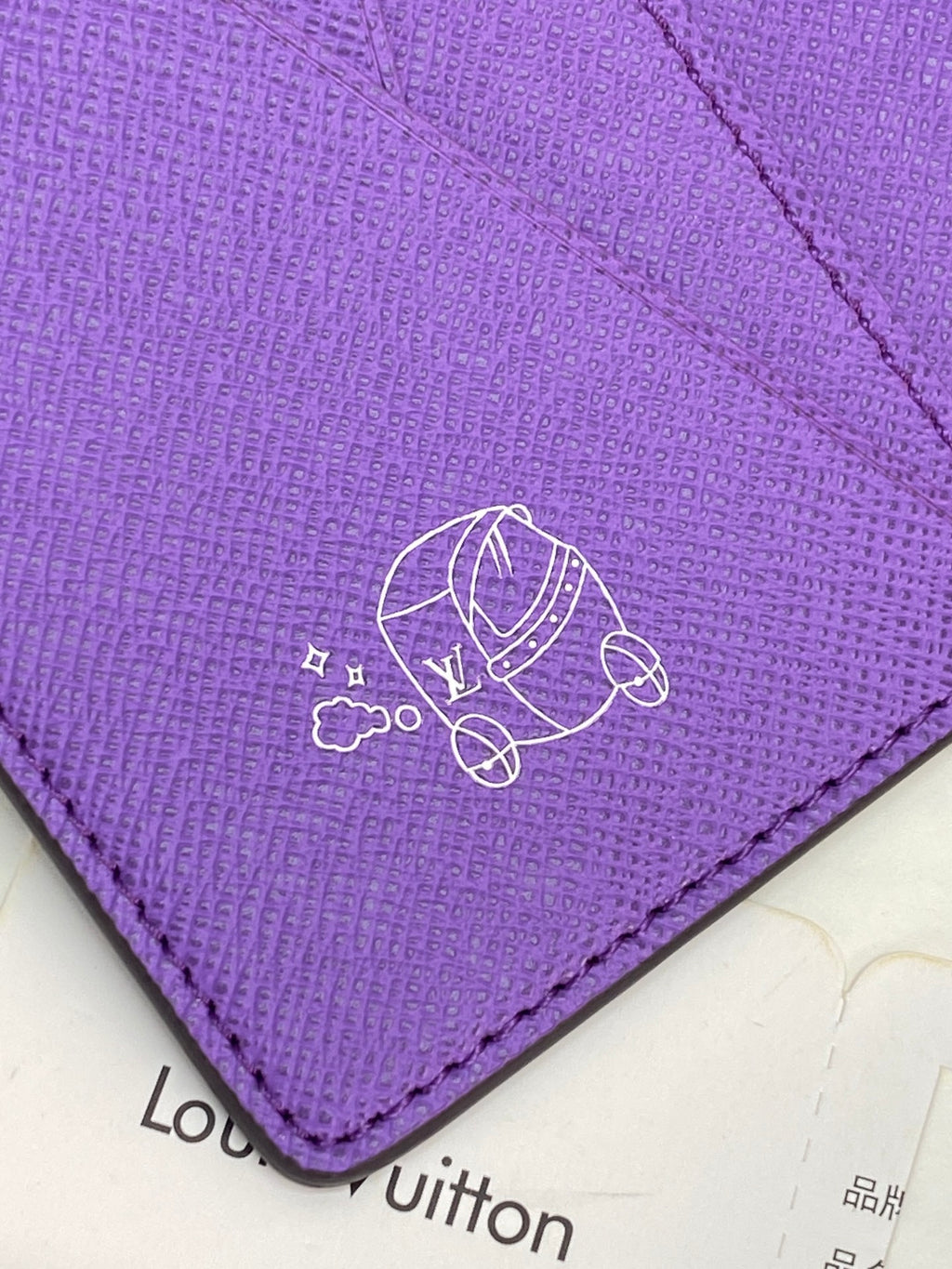 Small bag card holder close-up of purple flap with line art logo emblem