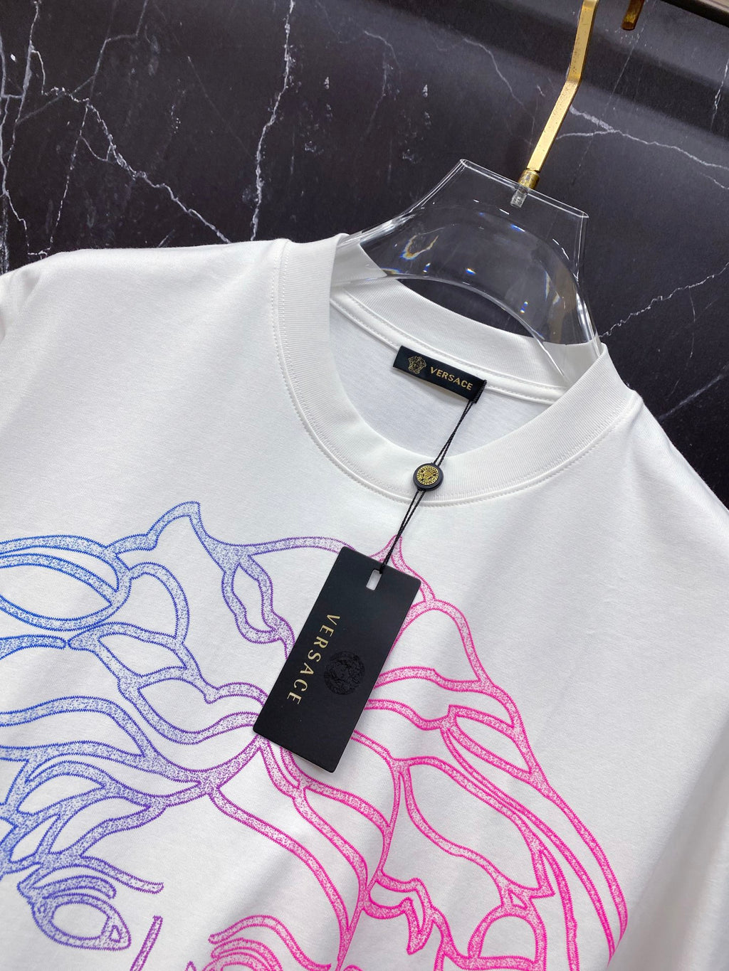 White T-shirt with blue and pink Medusa graphic and hanging Versace tag at collar.