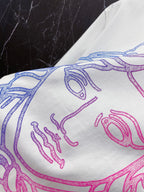White T-shirt close-up of blue and pink line-art face graphic.