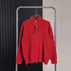 Red knit zip-up sweater with high collar and front zipper, hanging from rack