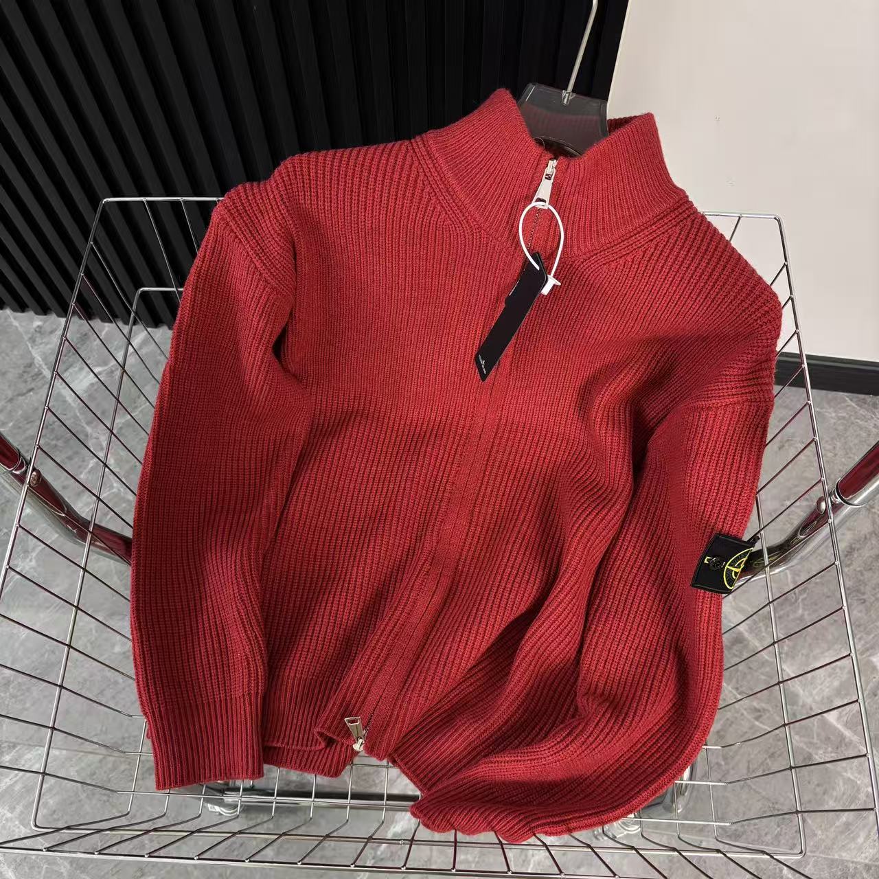 Red knit zip-up sweater with high collar and front zipper, draped on metal rack