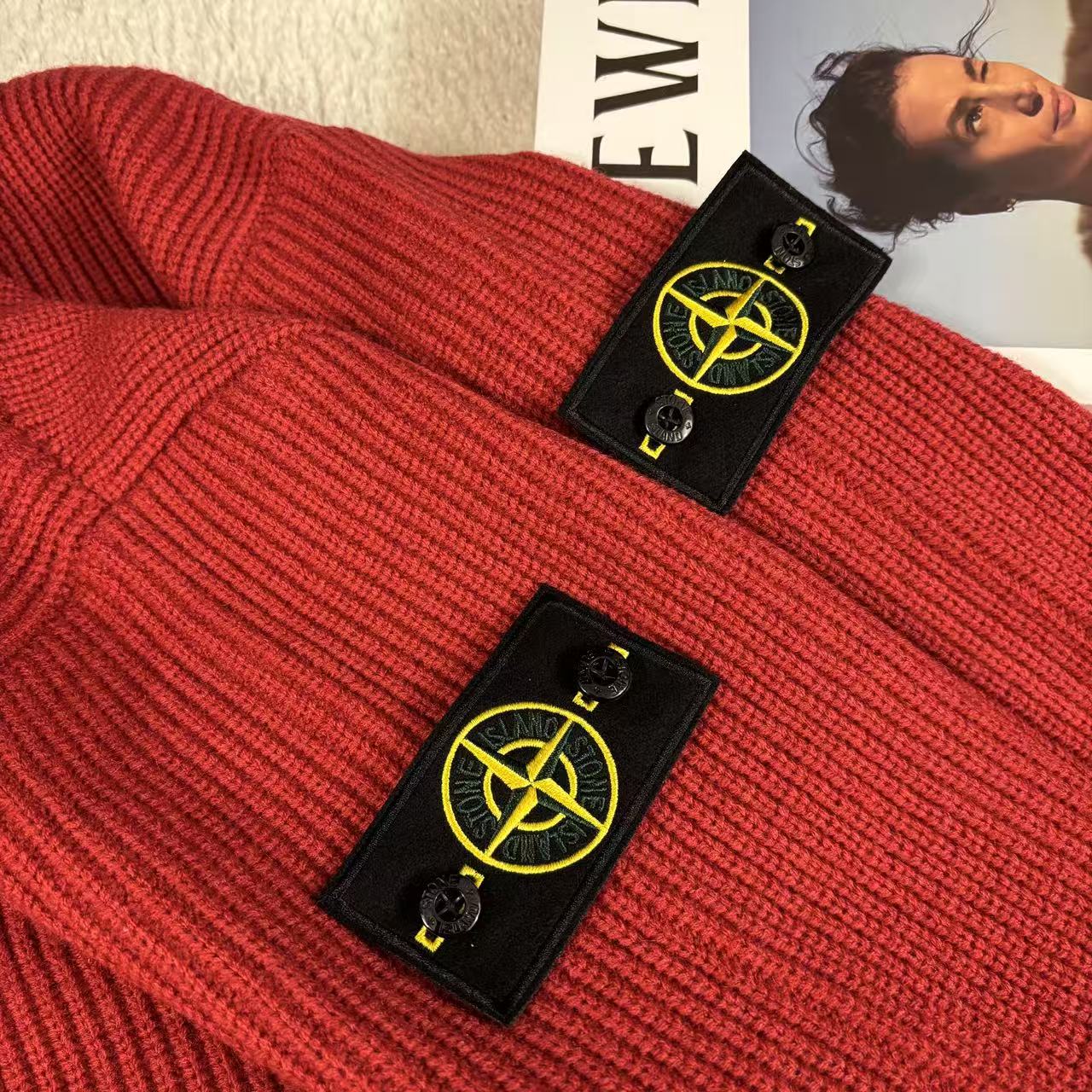 Red knit sweater lying flat with Stone Island branded hang tags near collar