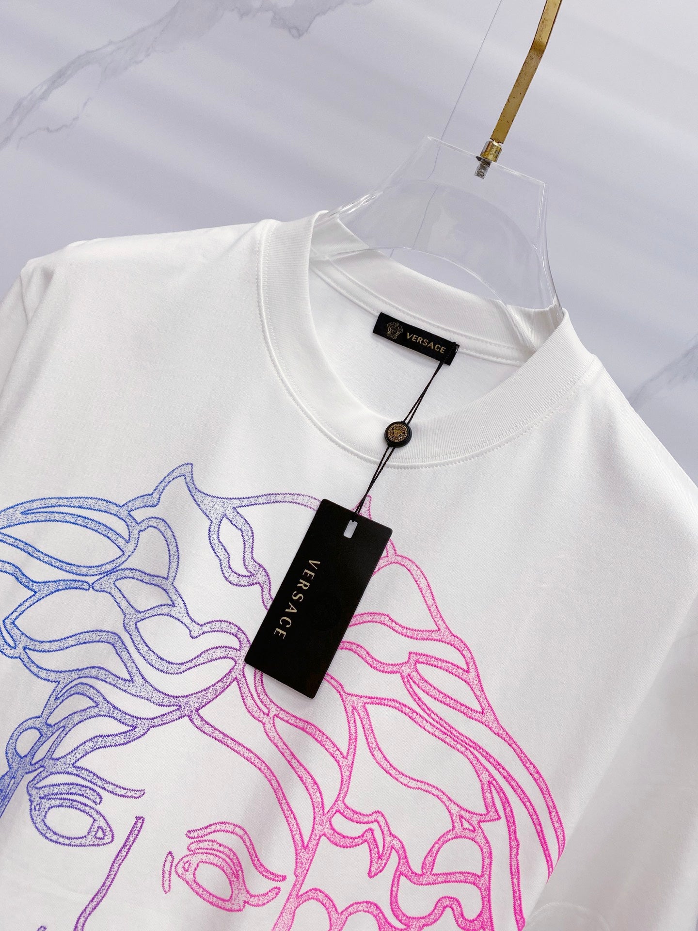 White crewneck T-shirt with hanging label and blue/pink Medusa graphic