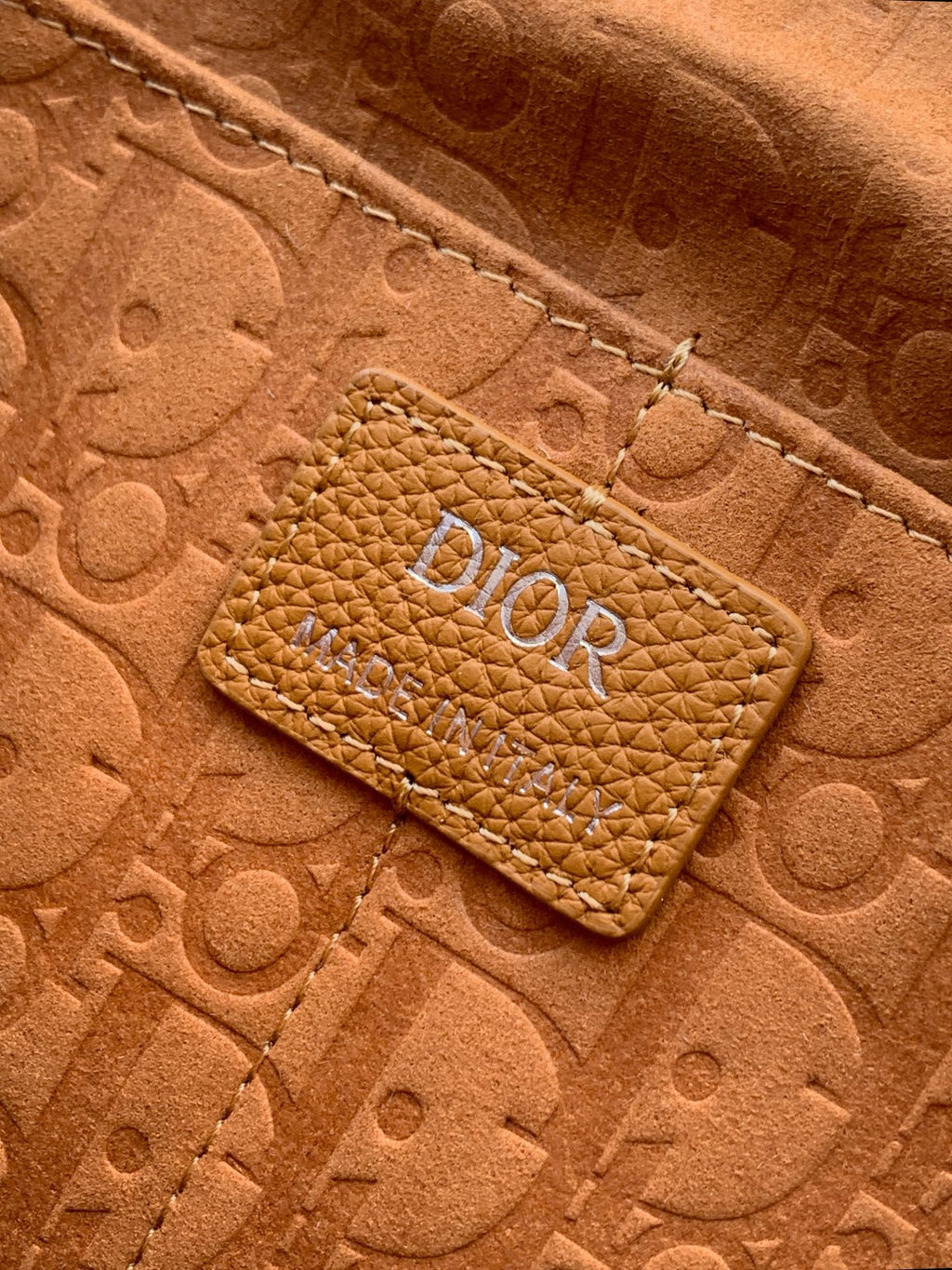 Close-up of tan leather bag logo patch on embossed monogram texture