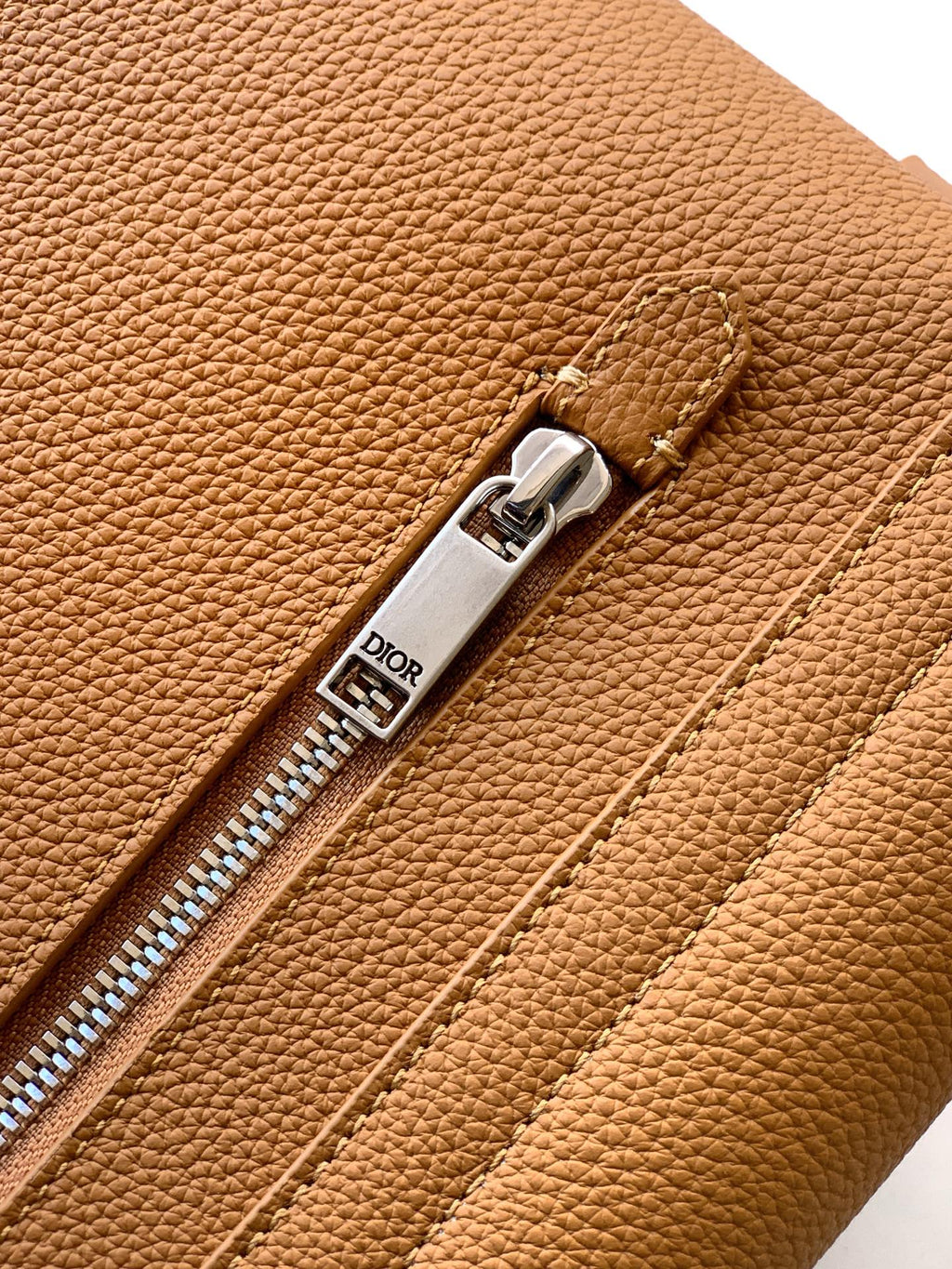 Close-up of tan leather zipper pull and stitched seam detail