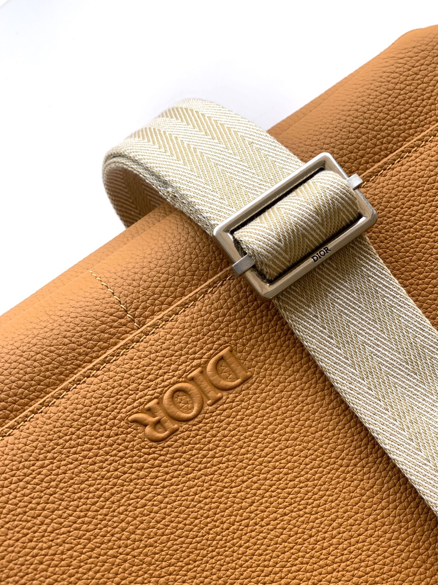 Close-up of tan leather belt strap with Dior logo buckle