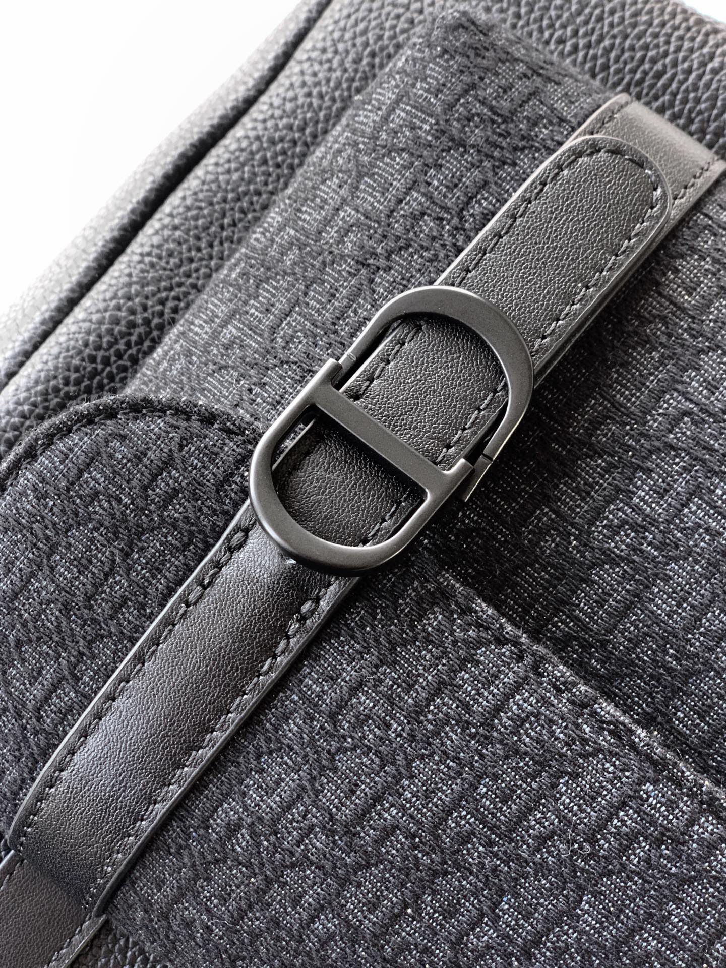 Dior backpack strap close-up with metal buckle and stitched textured leather.