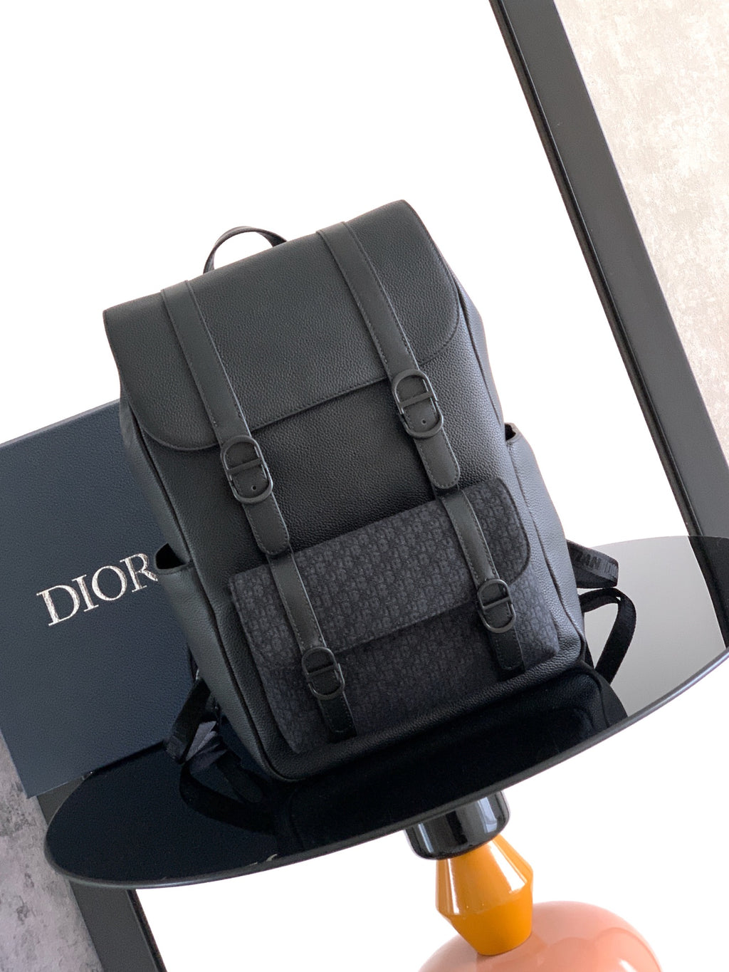 Dior backpack with flap and buckles, textured dark leather, top handle and shoulder straps.