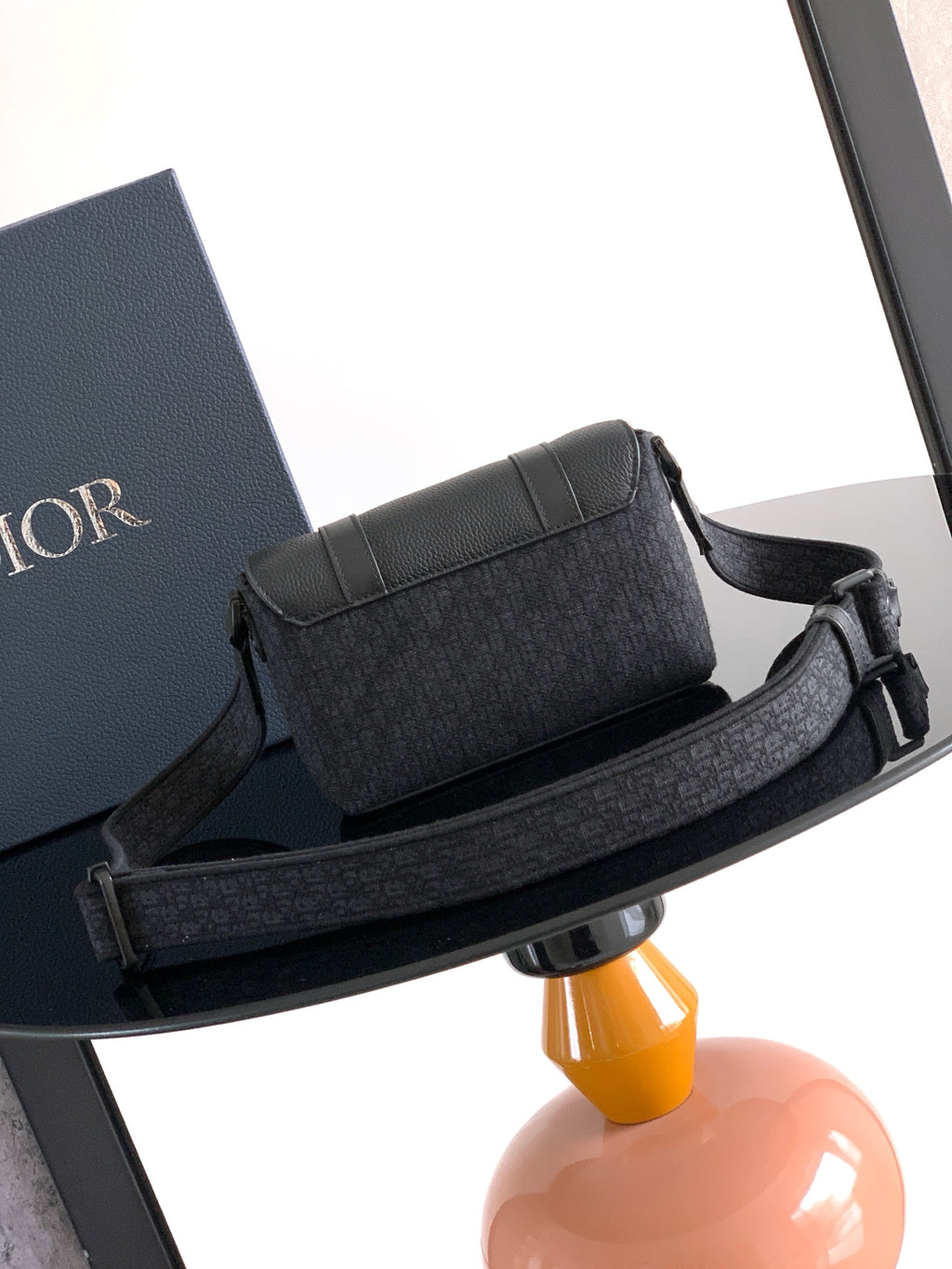 Dior bag with structured flap, dark textured exterior, and adjustable strap with buckle.
