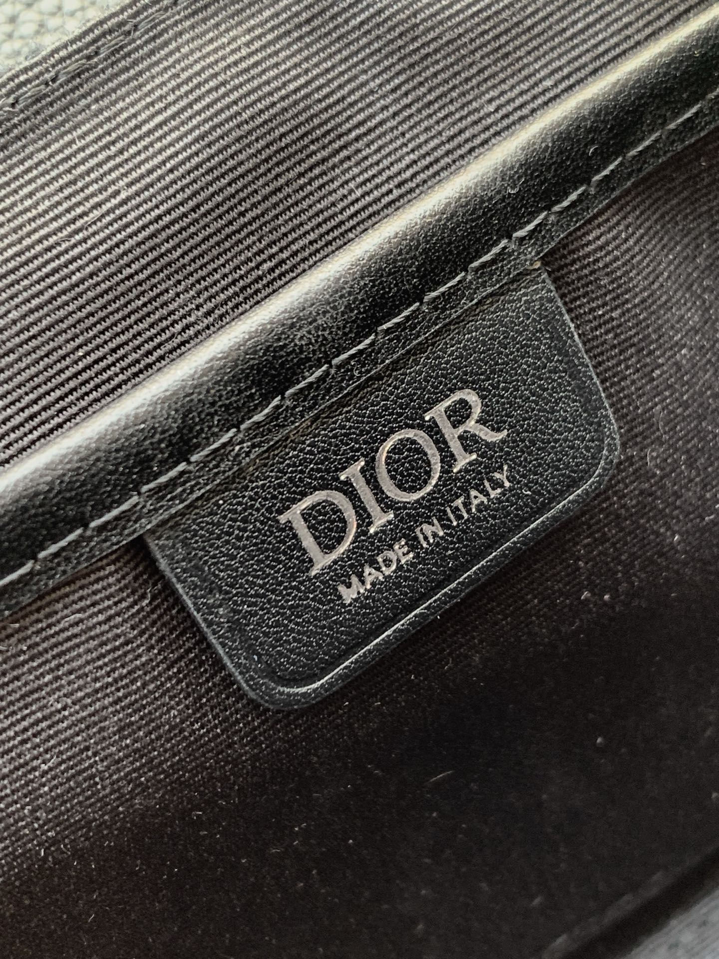 Dior bag leather patch with “DIOR” logo on dark textured fabric.