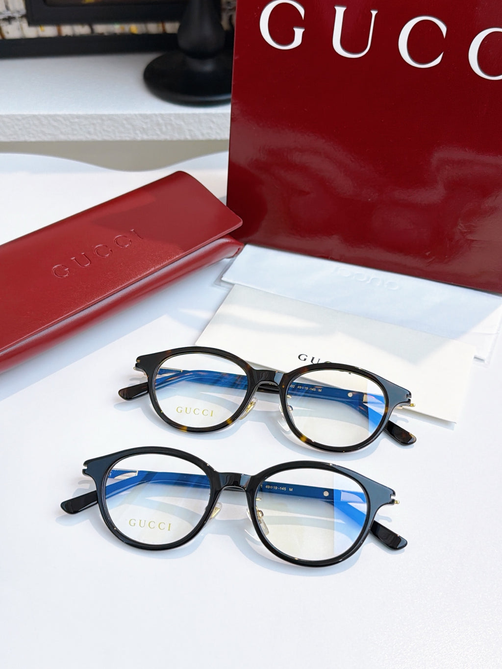 Gucci eyeglasses, black round frames with blue-tinted lenses; two pairs shown