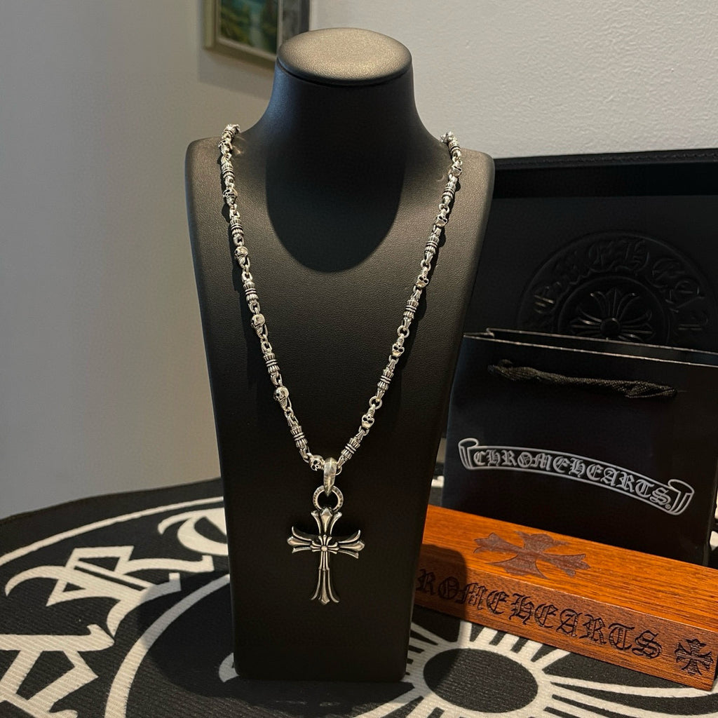 Silver cross pendant necklace with layered chain on black display bust