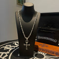 Silver cross pendant necklace with layered chain on black display bust