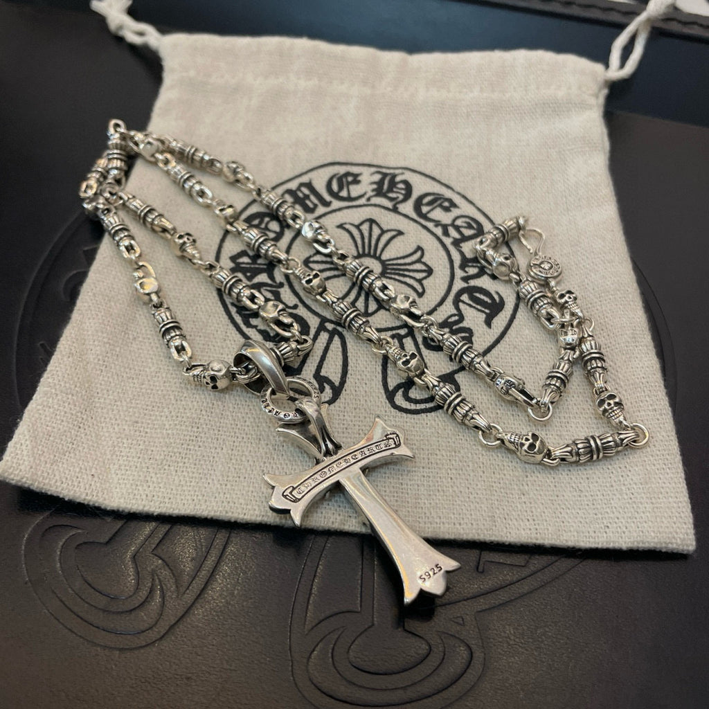 Silver cross pendant necklace resting on cream drawstring pouch on dark surface
