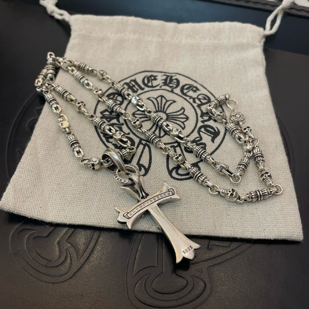 Silver cross pendant necklace resting on cream drawstring pouch on dark surface