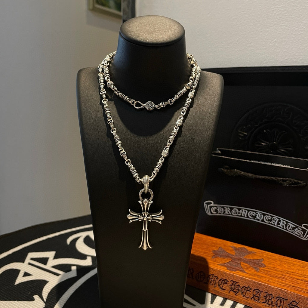 Silver cross pendant necklace with multiple chain strands on black display bust