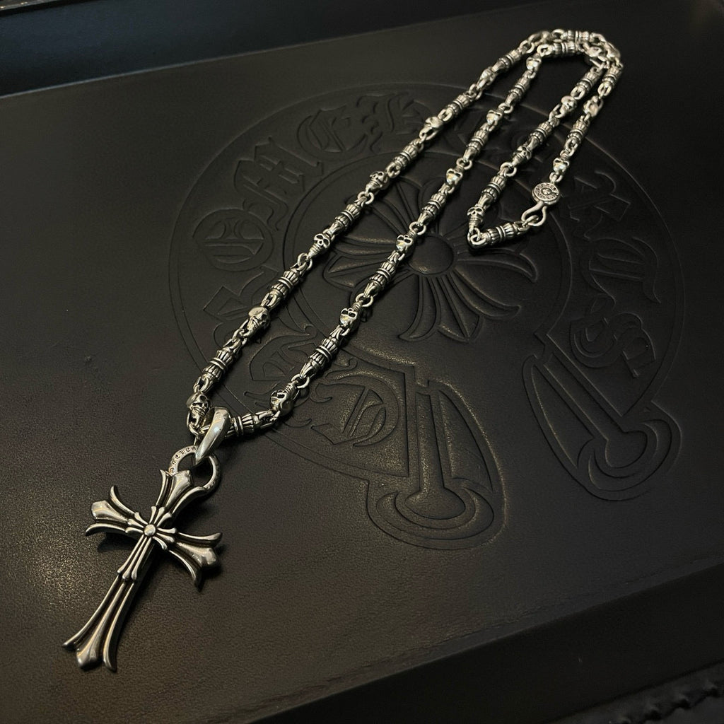 Silver cross pendant necklace detail on embossed dark box, close-up