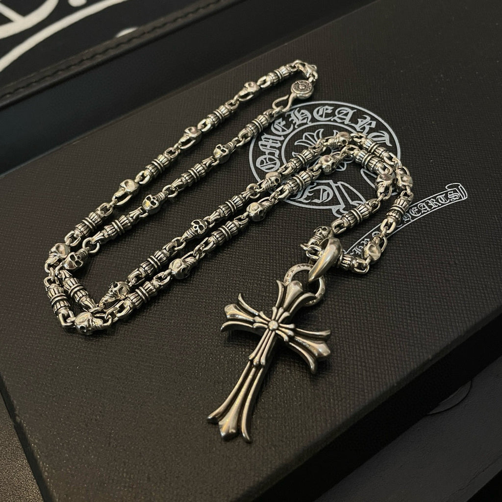 Silver cross pendant necklace and chain set on dark leather box with logo