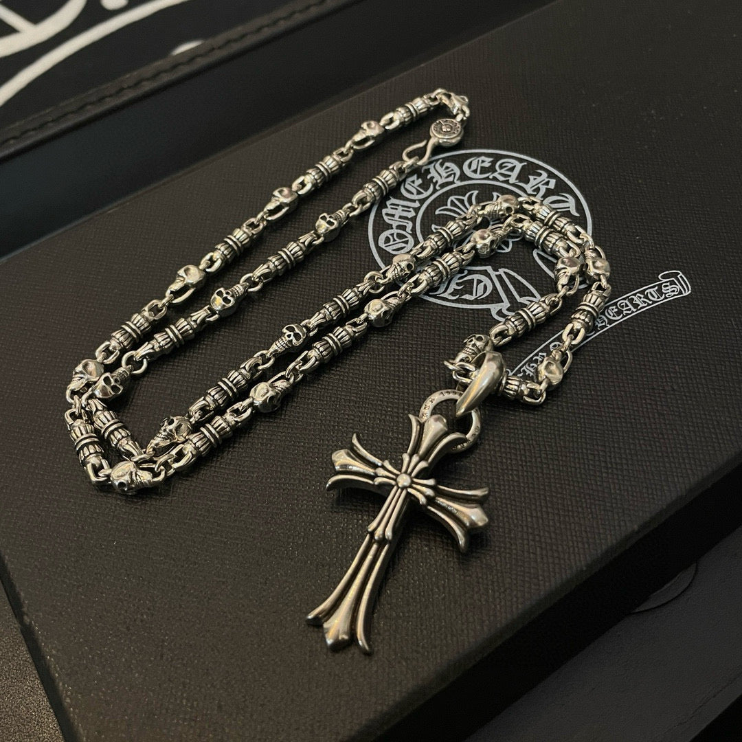 Silver cross pendant necklace and chain set on dark leather box with logo