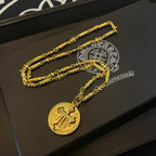 Gold-tone cross pendant necklace with round pendant on black jewelry box base.