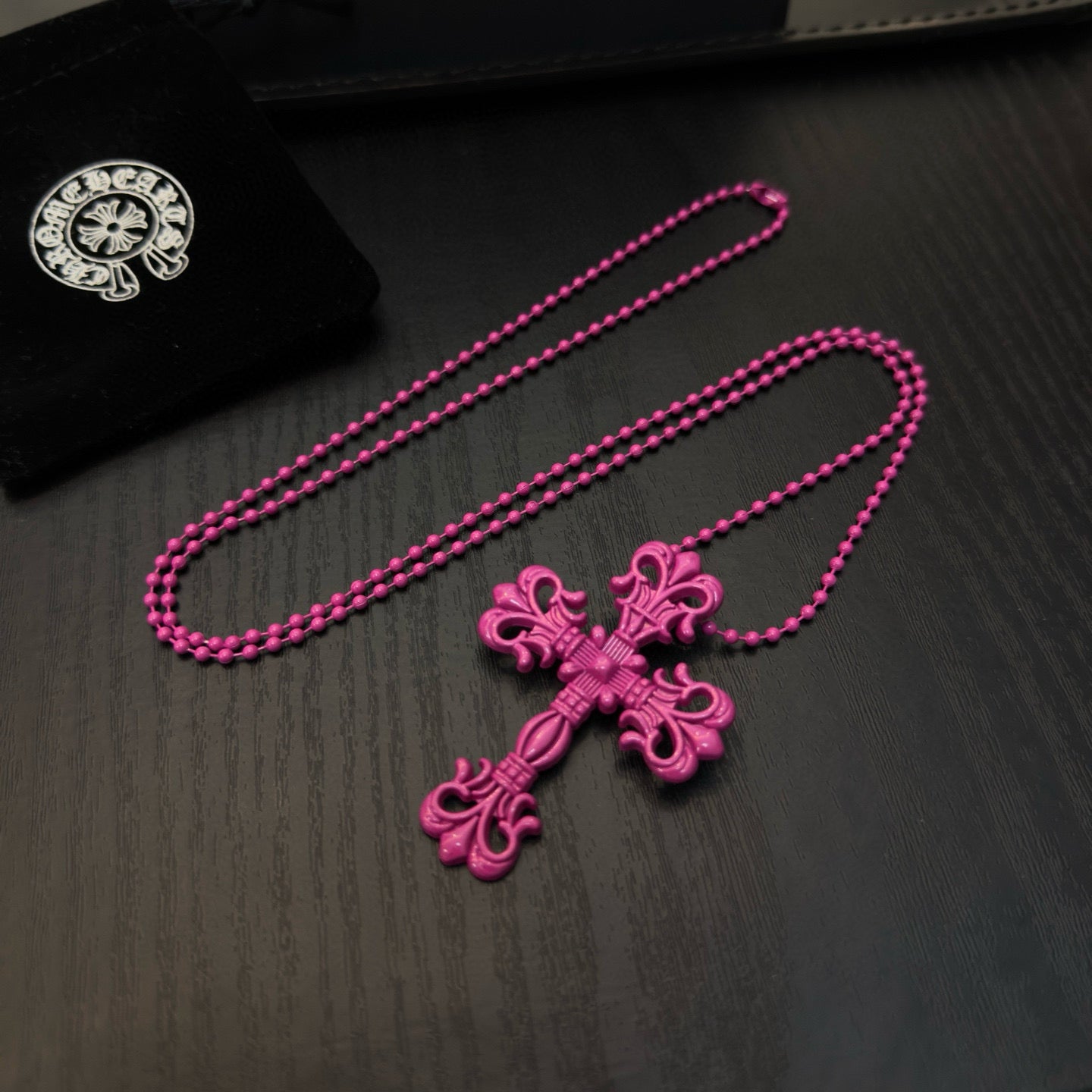 Pink beaded cross necklace with floral cross pendant, laid on a dark surface