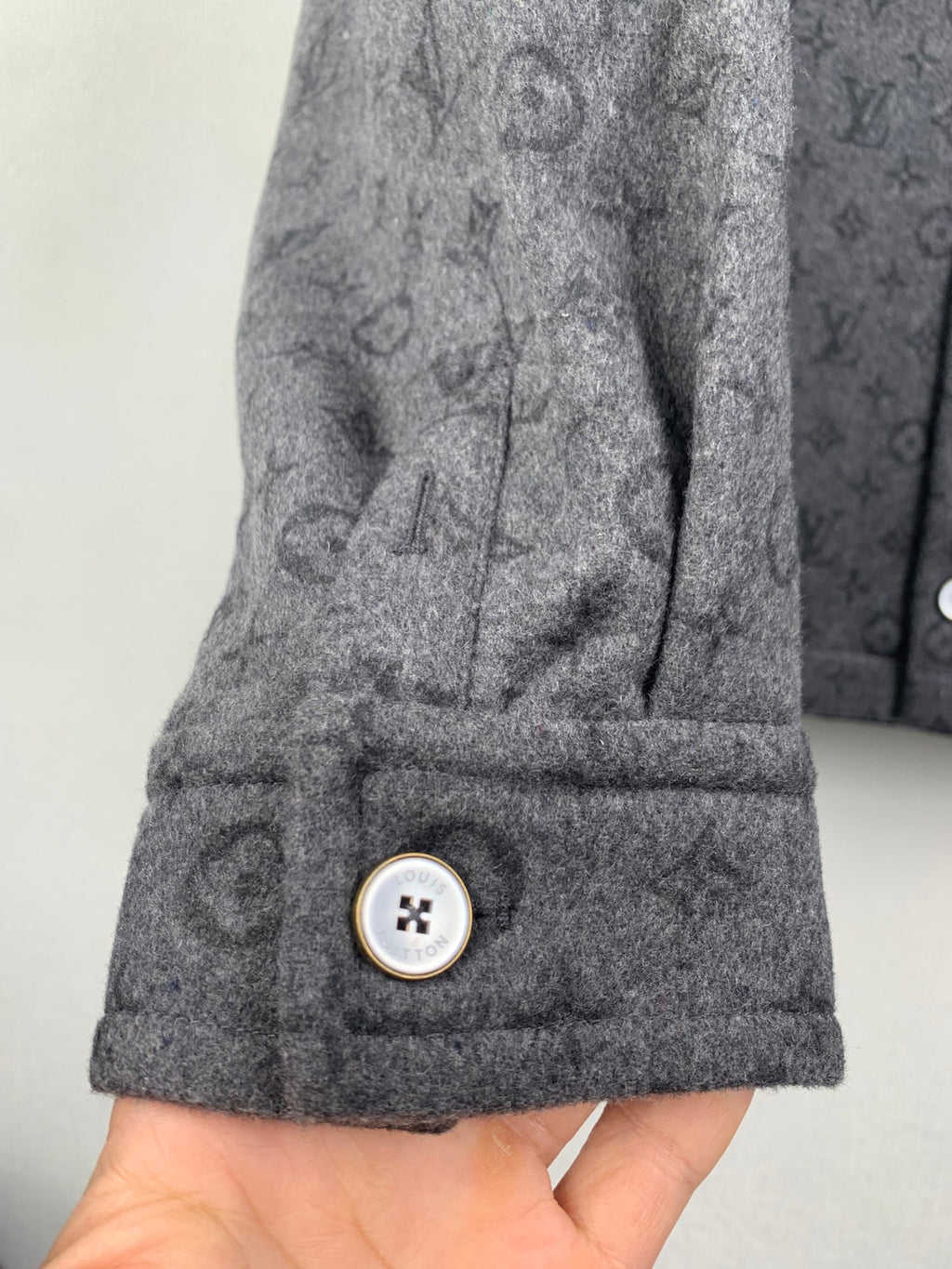 Monogram button-up shirt cuff close-up with gold-trimmed snap button