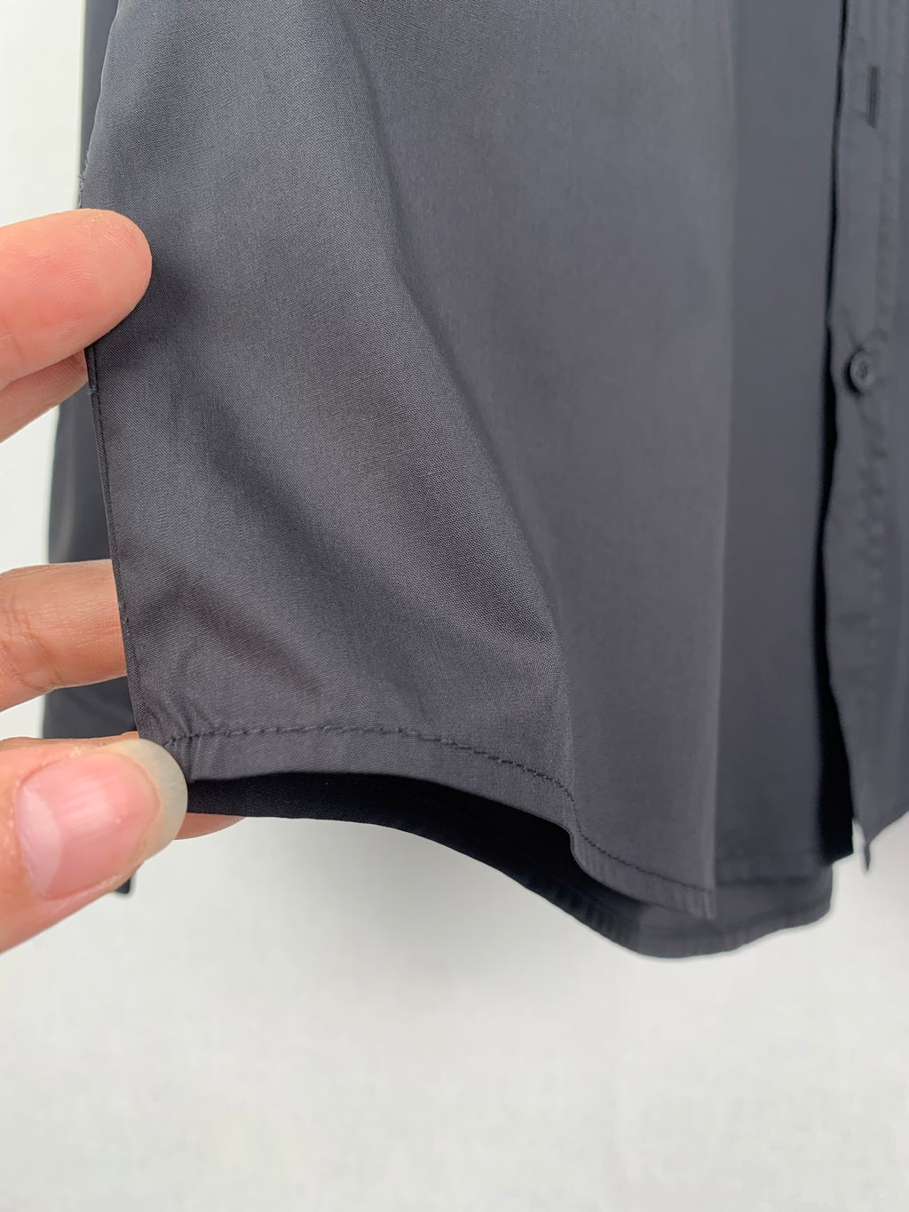 Long-sleeve button-up shirt, dark gray, hand-held view of side hem and seam