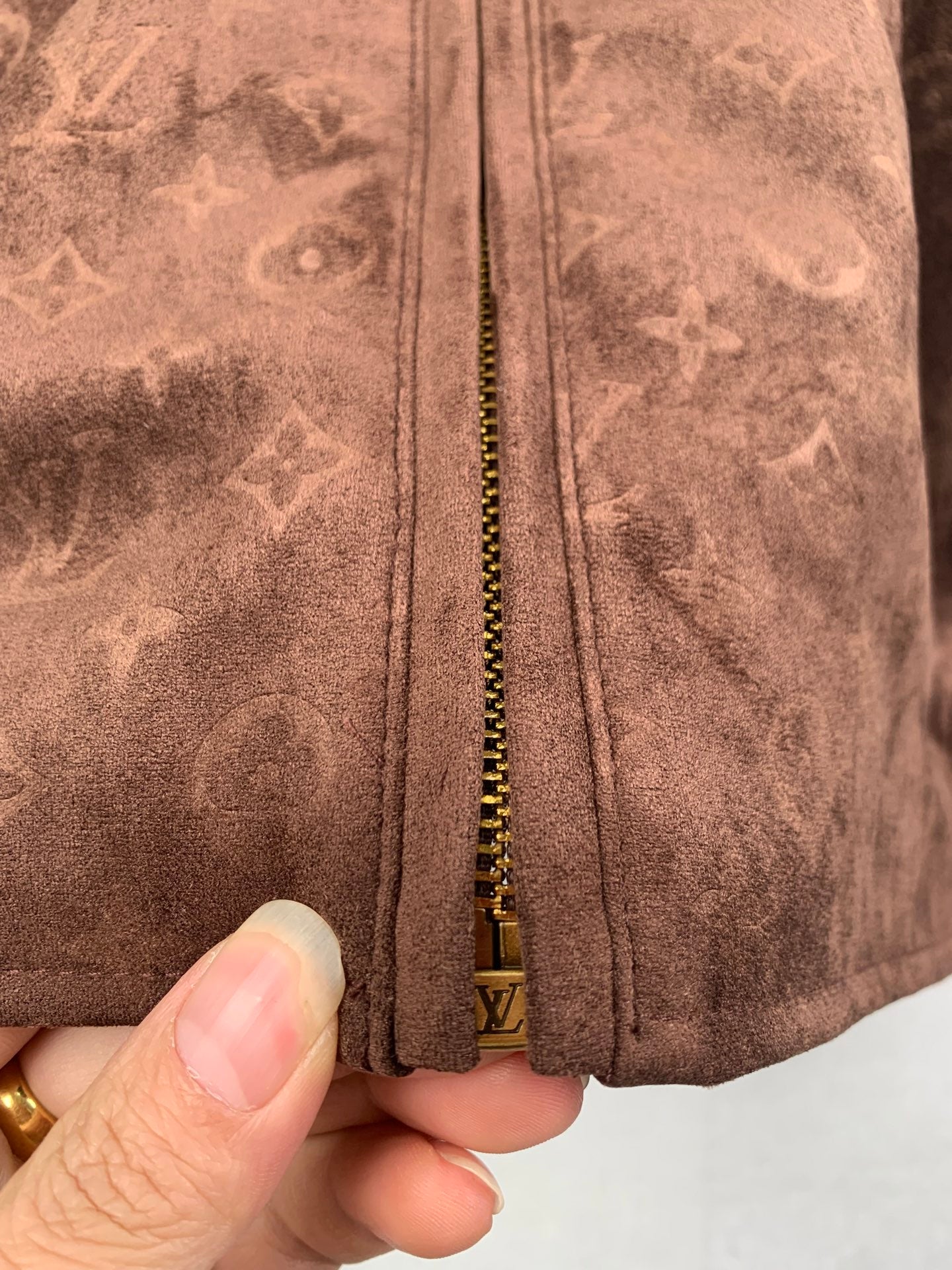 Dark brown monogram jacket zipper close-up with gold chain and pull tab