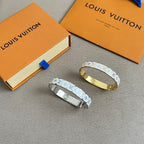 Gold and silver Louis Vuitton cuff bracelets with LV monogram pattern, laid on gray