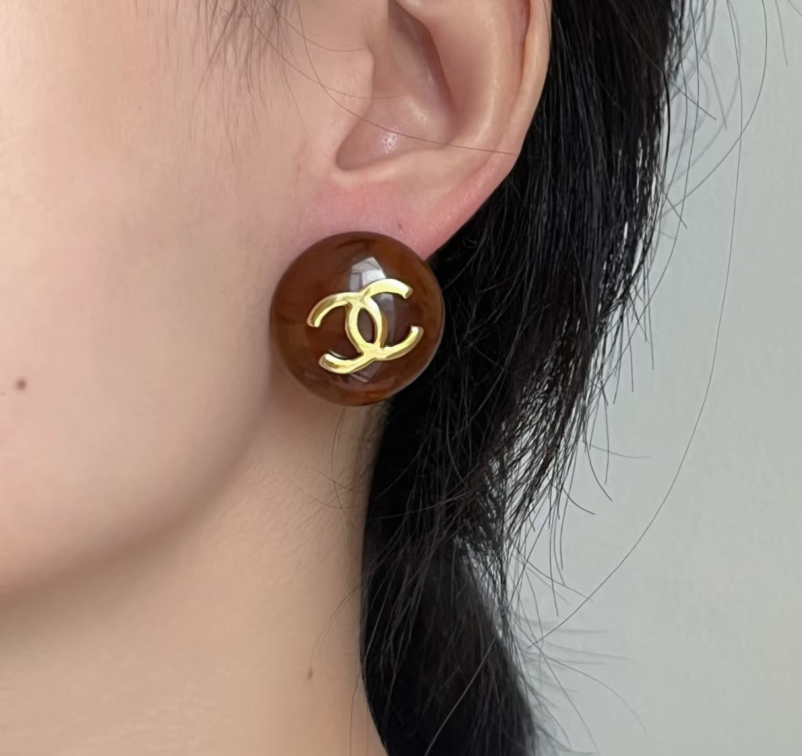 Brown round stud earrings with gold-tone Chanel CC logo on model ear