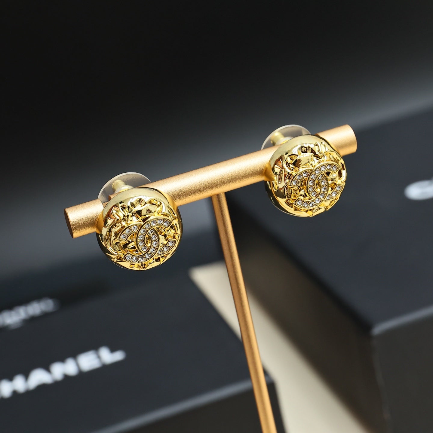 Gold-tone stud earrings with round logo face on a display stand