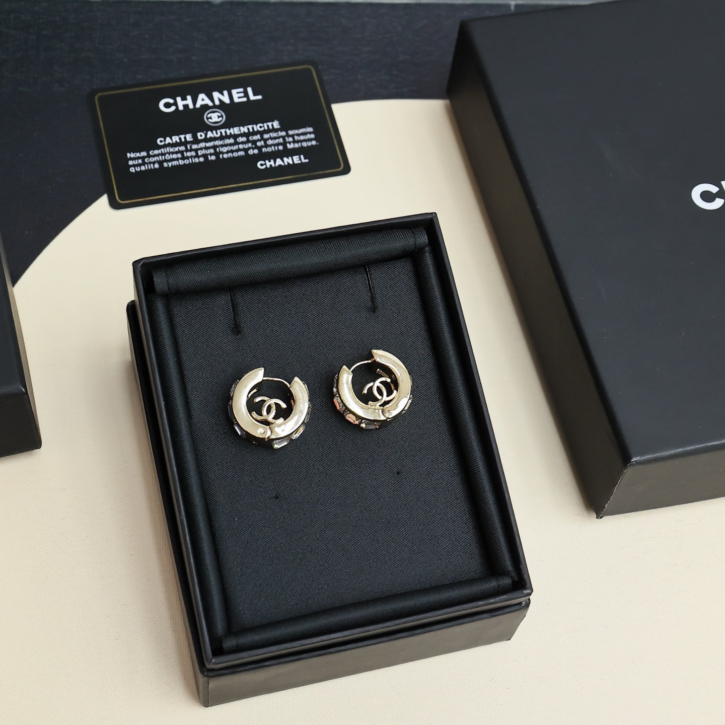 Gold-tone hoop earrings with logo medallion and clear rhinestone accents in box