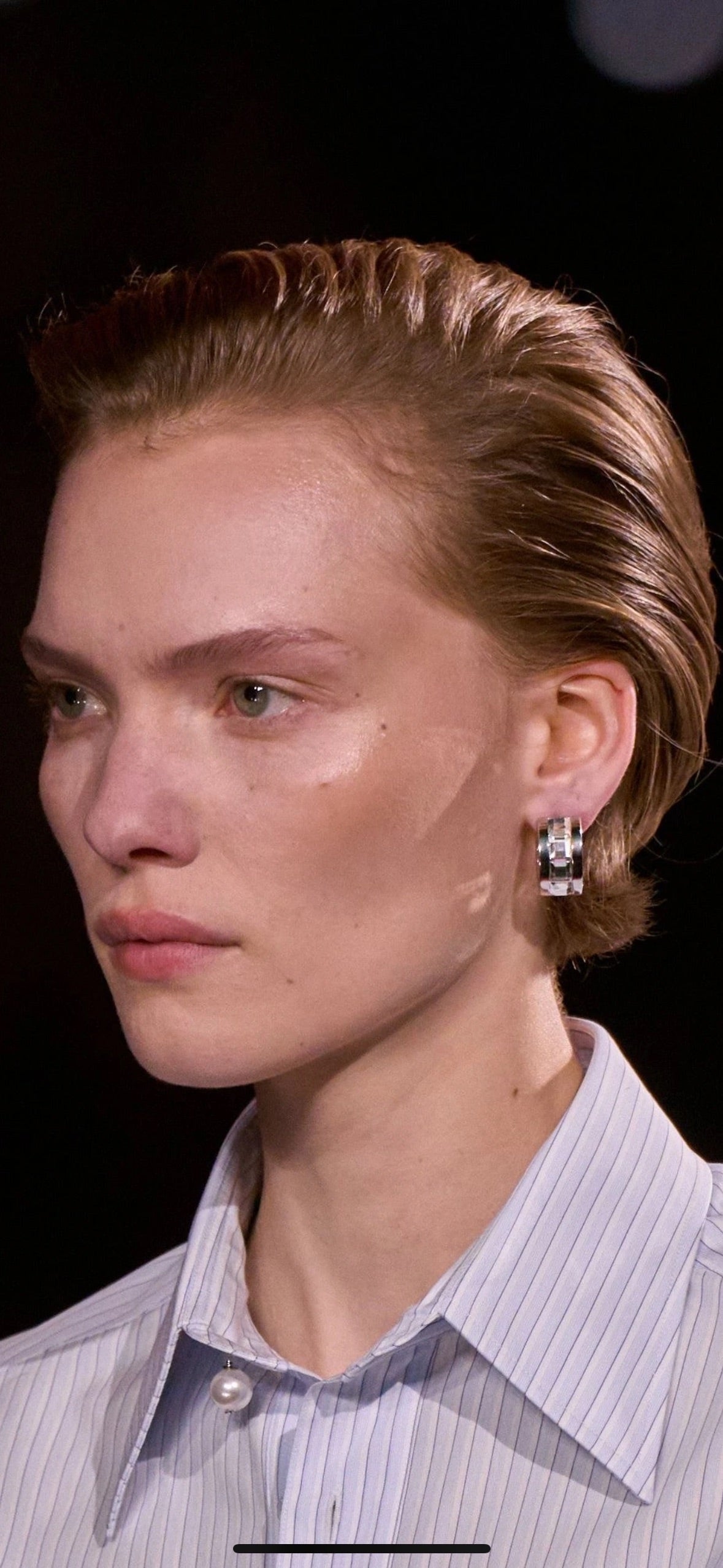 Gold-tone hoop earrings with clear rhinestone accents worn on the ear