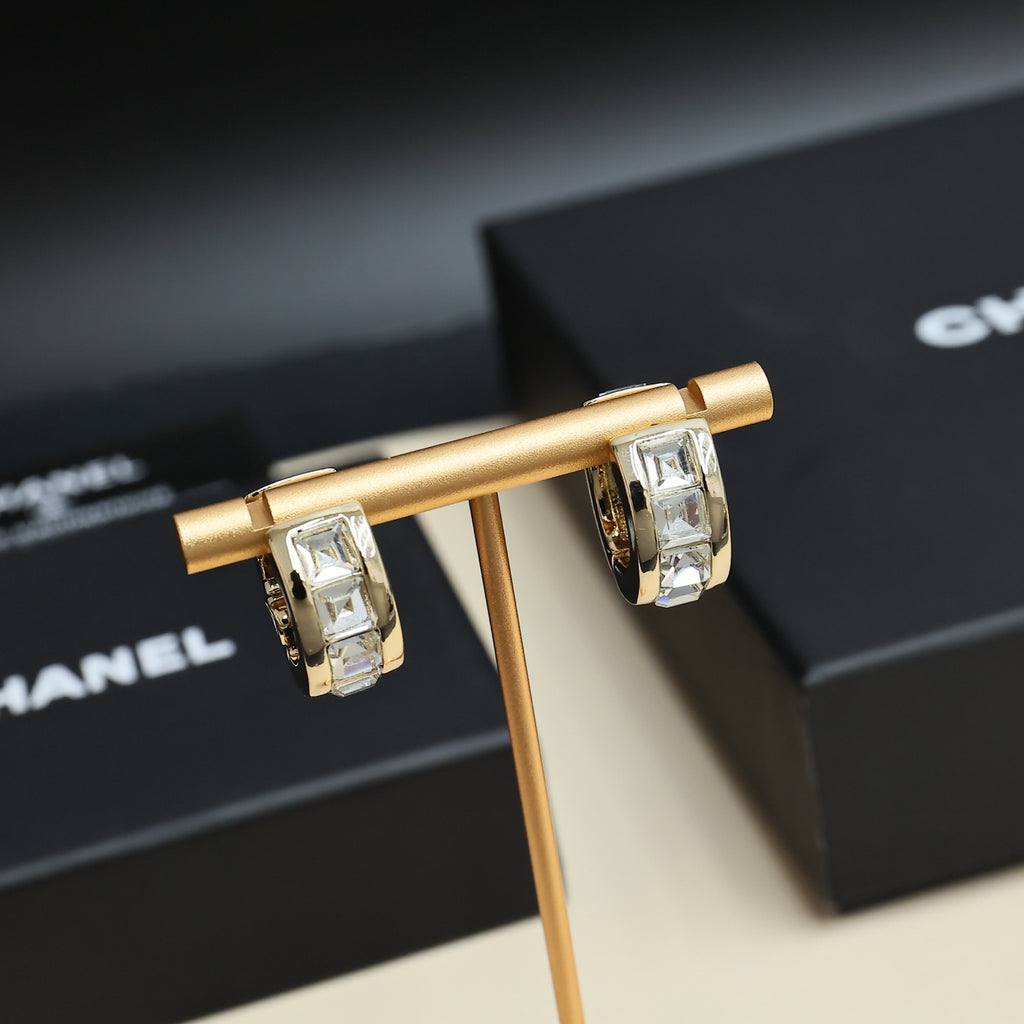Gold-tone hoop earrings with interlocking logo and clear rhinestone stones, close-up