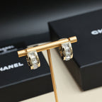 Gold-tone hoop earrings with interlocking logo and clear rhinestone stones, close-up