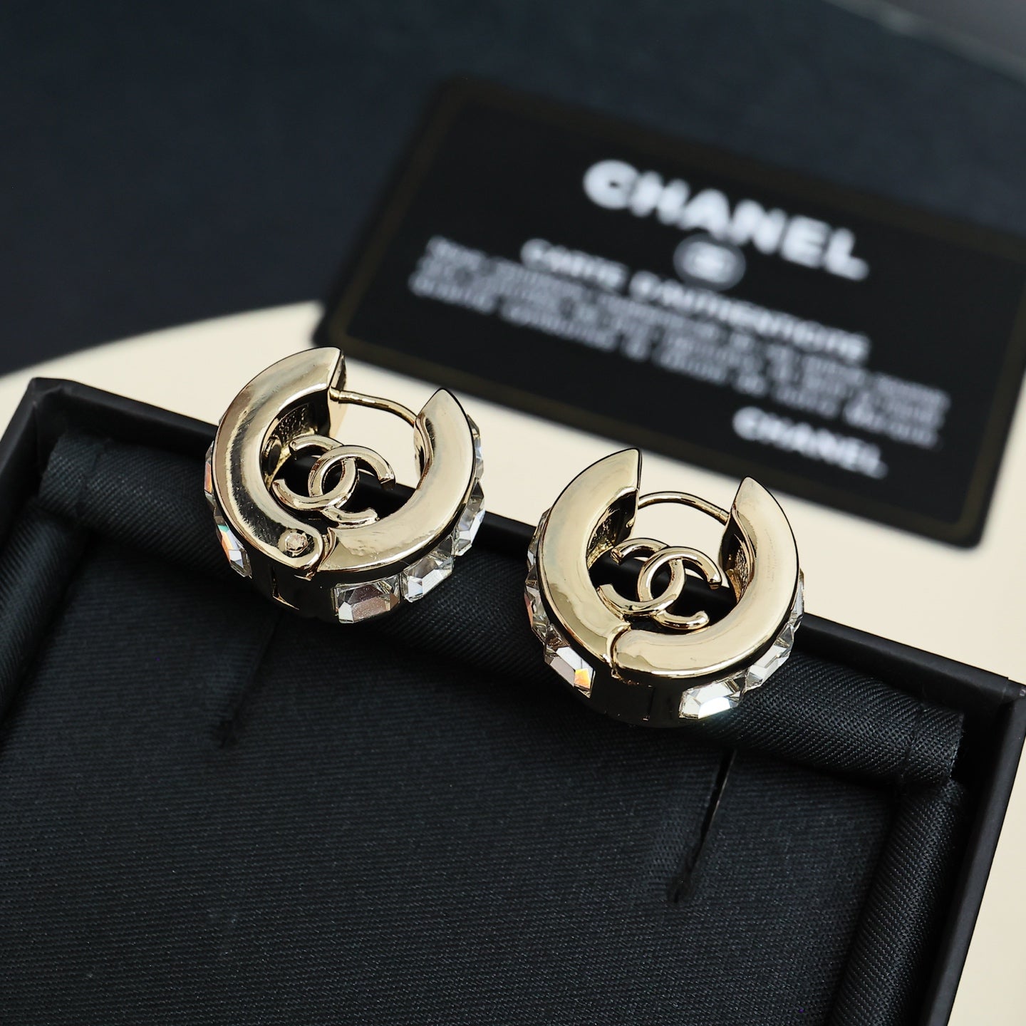 Gold-tone hoop earrings with interlocking logo center and clear stone embellishments