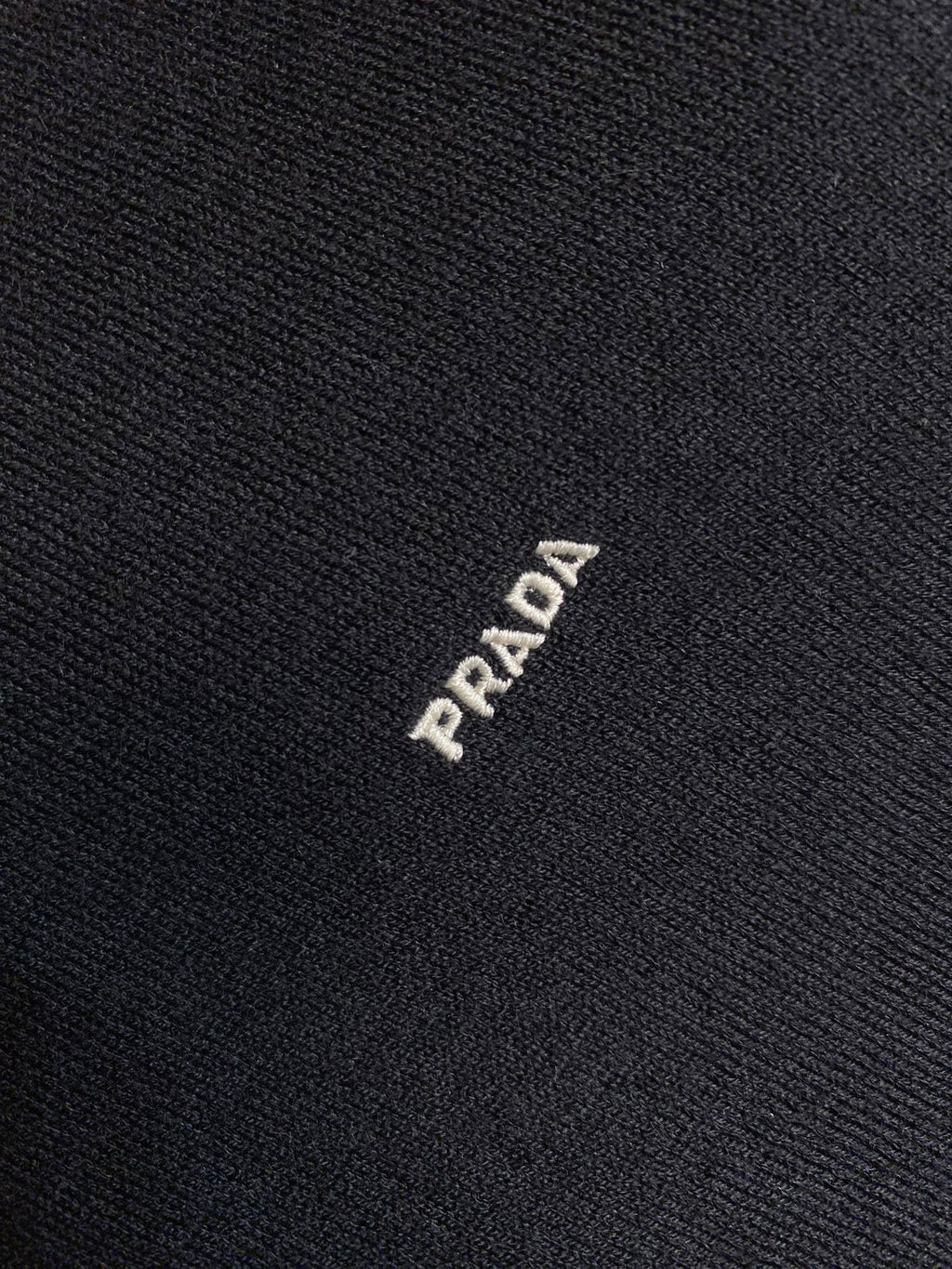 Dark knit sweater fabric with small PRADA logo stitch