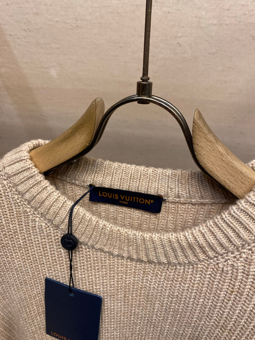 Cream knit sweater collar with Louis Vuitton size tag hanging on wooden hanger
