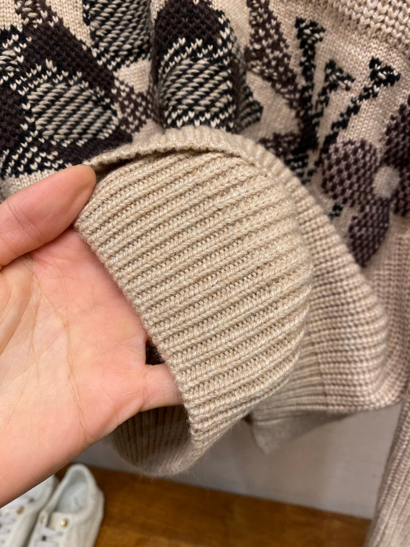 Cream knit sweater cuff with ribbed knit texture and dark patterned panel behind