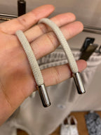 Cream drawstring cords with metal aglets, looped through waistband
