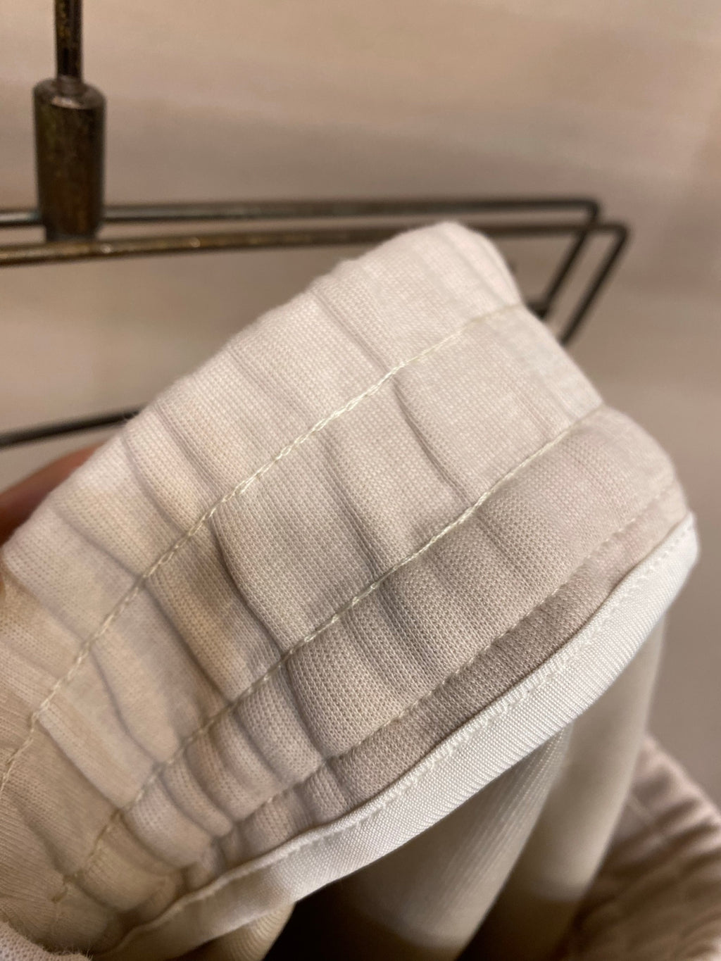 Light cream pants fabric close-up with ribbed knit waistband and stitched hem